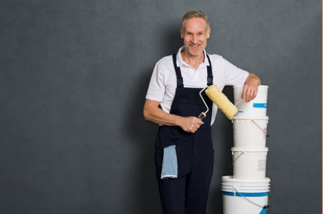 Mature smiling Granby professional painter with a roller in his right hand and his left arm resting on paint buckets.