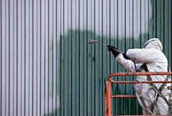 Pintor profesional en Granby usando equipo de protección total en una góndola. Pinta el revestimiento de un edificio de metal.
